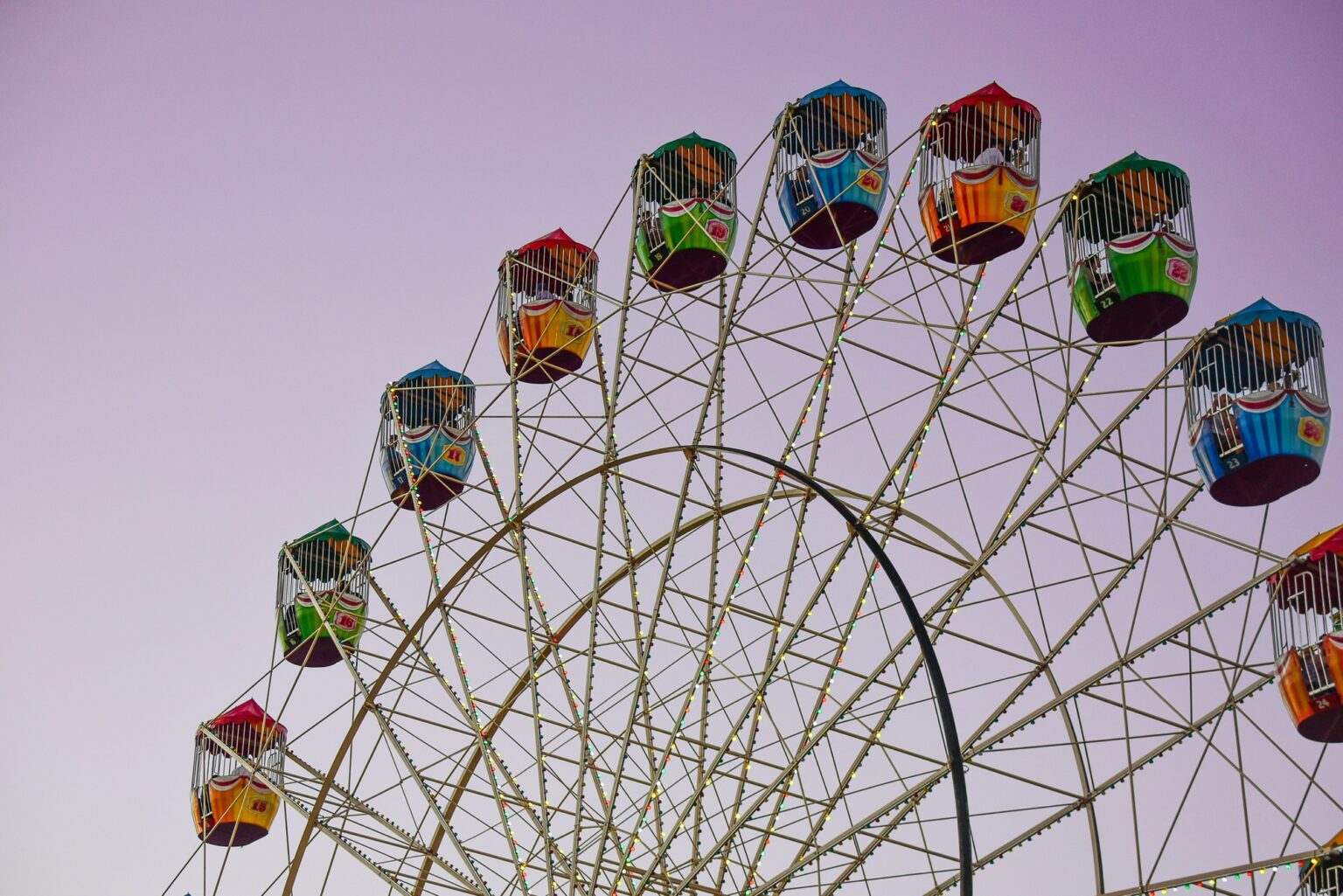 A Ferris wheel at an amusement park against a mauve sky at sunset